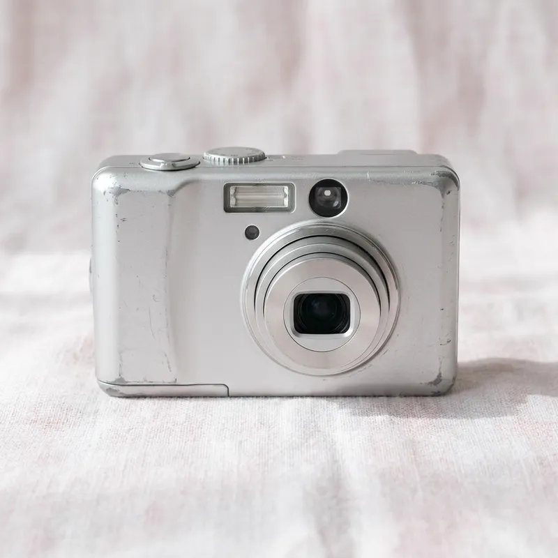 Generated image: a silver compact digital camera with worn edges on pale linen